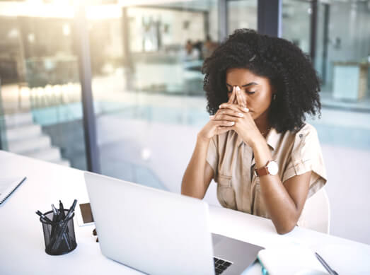 Frustrated employee sitting at desk with hands on head.